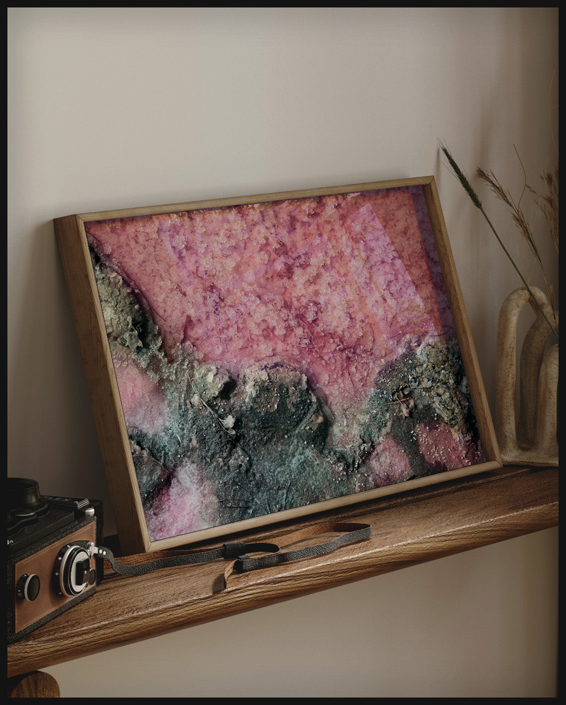 Ein gerahmtes Poster von rosa Salz und dunklem Gestein, auf einem Holzregal an die Wand angelehnt