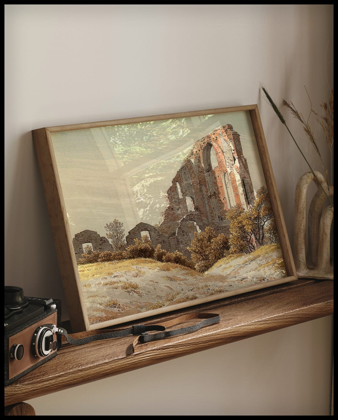 Ein gerahmter Kunstdruck von einer alten Ruine hinter einem grasbewachsenen Hügel, auf einem Holzregal an die Wand angelehnt