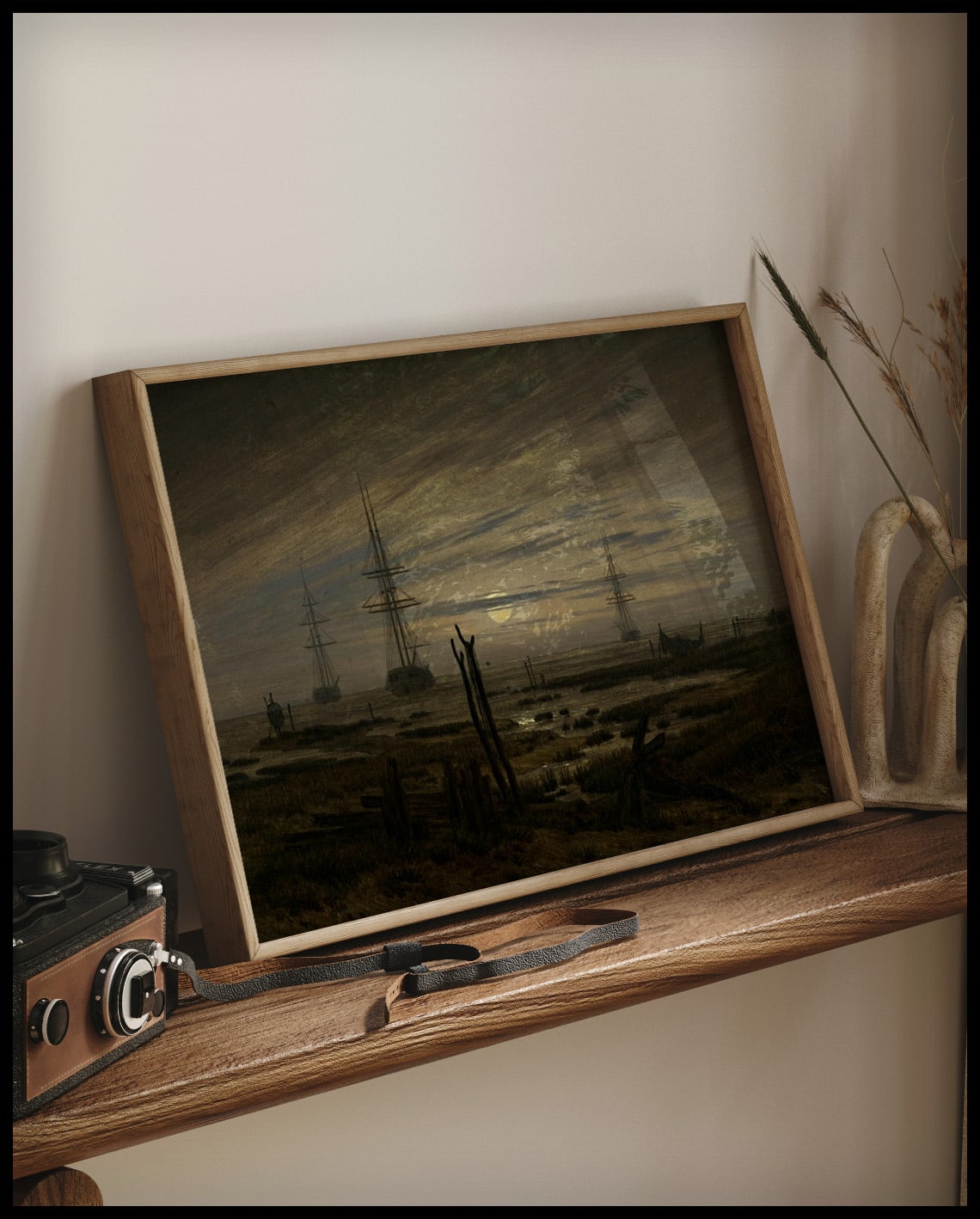 Ein gerahmter Kunstdruck von drei Segelschiffen auf der Reede im Mondschein, auf einem Holzregal an die Wand angelehnt
