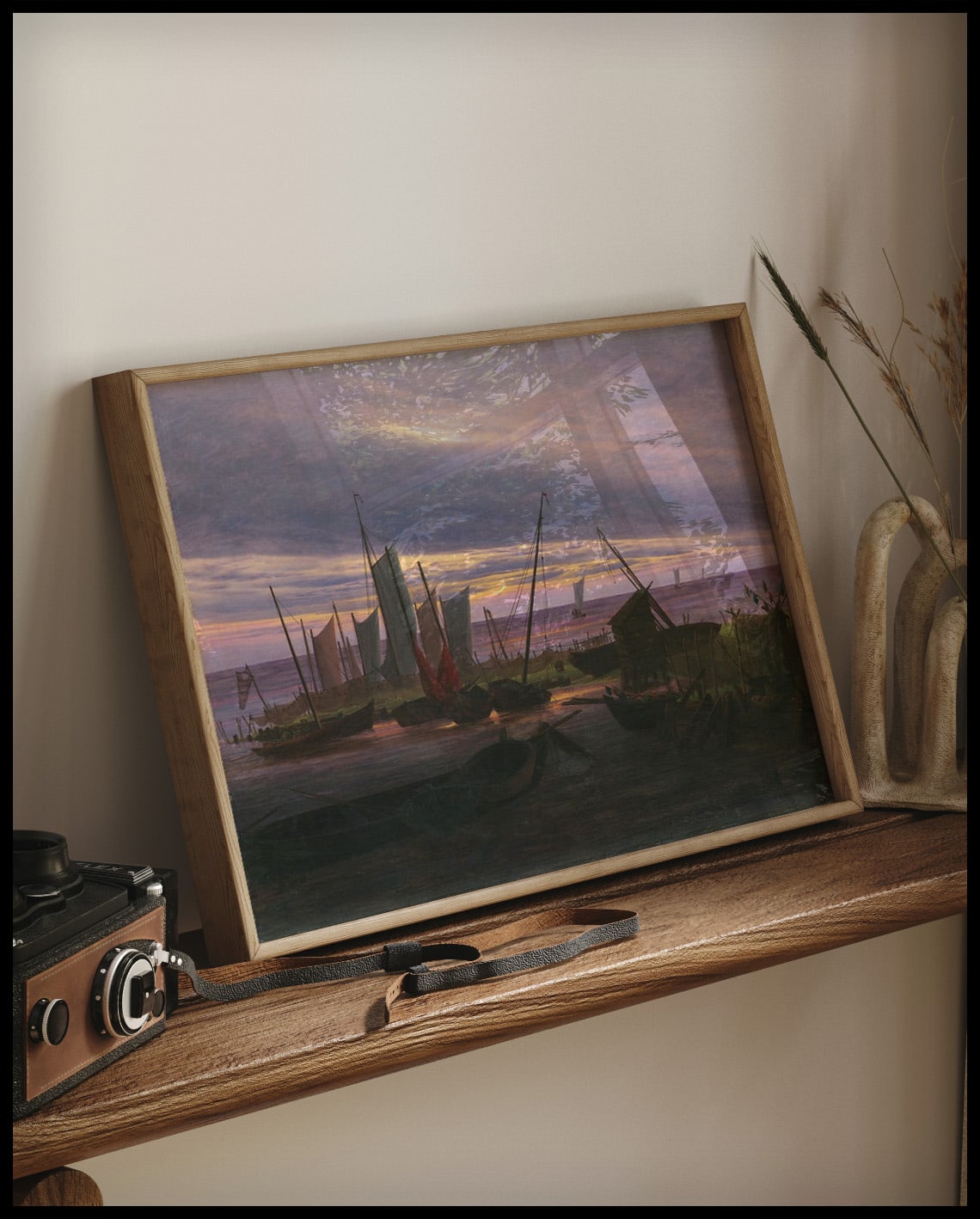 Ein gerahmter Kunstdruck von mehreren Holzbooten in einem kleinen Hafen am Abend, auf einem Holzregal an die Wand angelehnt