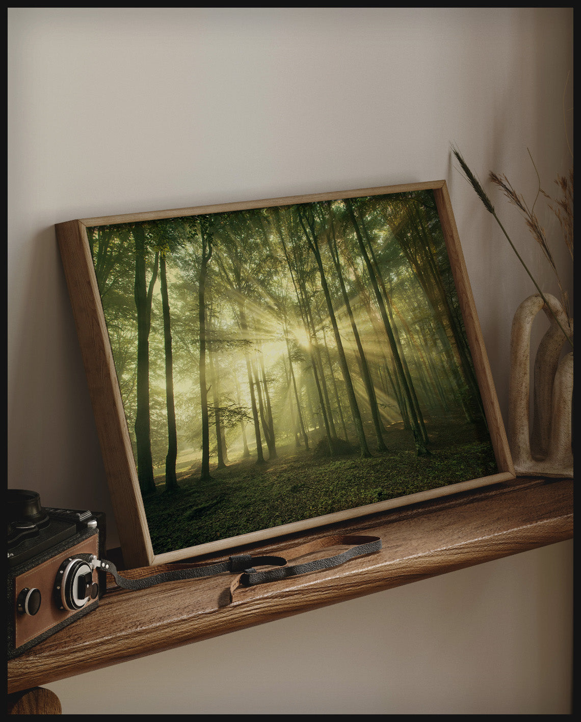 Ein gerahmtes Poster von Sonnenstrahlen die in einem Wald durch schmale Bäume hindurch scheinen, auf einem Holzregal an die Wand angelehnt