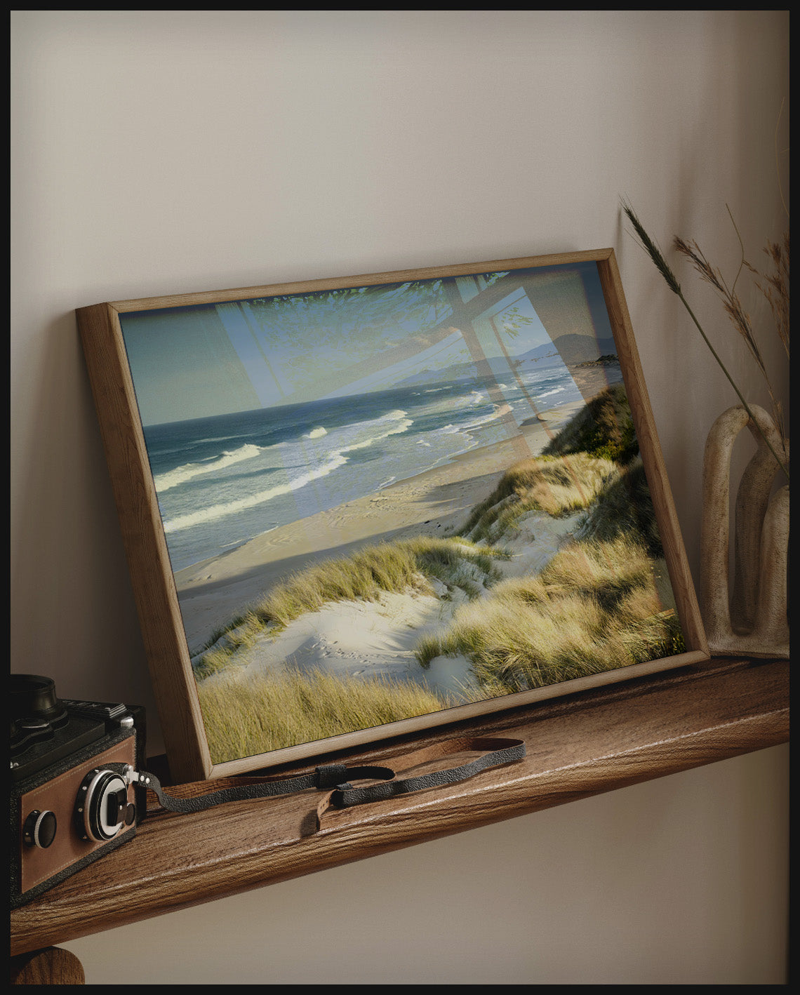 Ein gerahmtes Poster vom Meerblick über Dünen und Strand, auf einem Holzregal an die Wand angelehnt