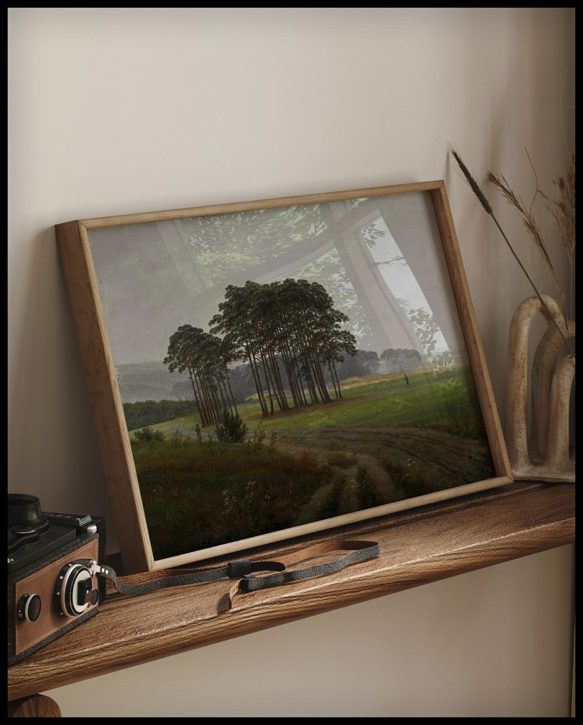 Ein gerahmter Kunstdruck von einer nebligen Wiese, einem Pfad und einem Wald im Hintergrund, auf einem Holzregal an die Wand angelehnt