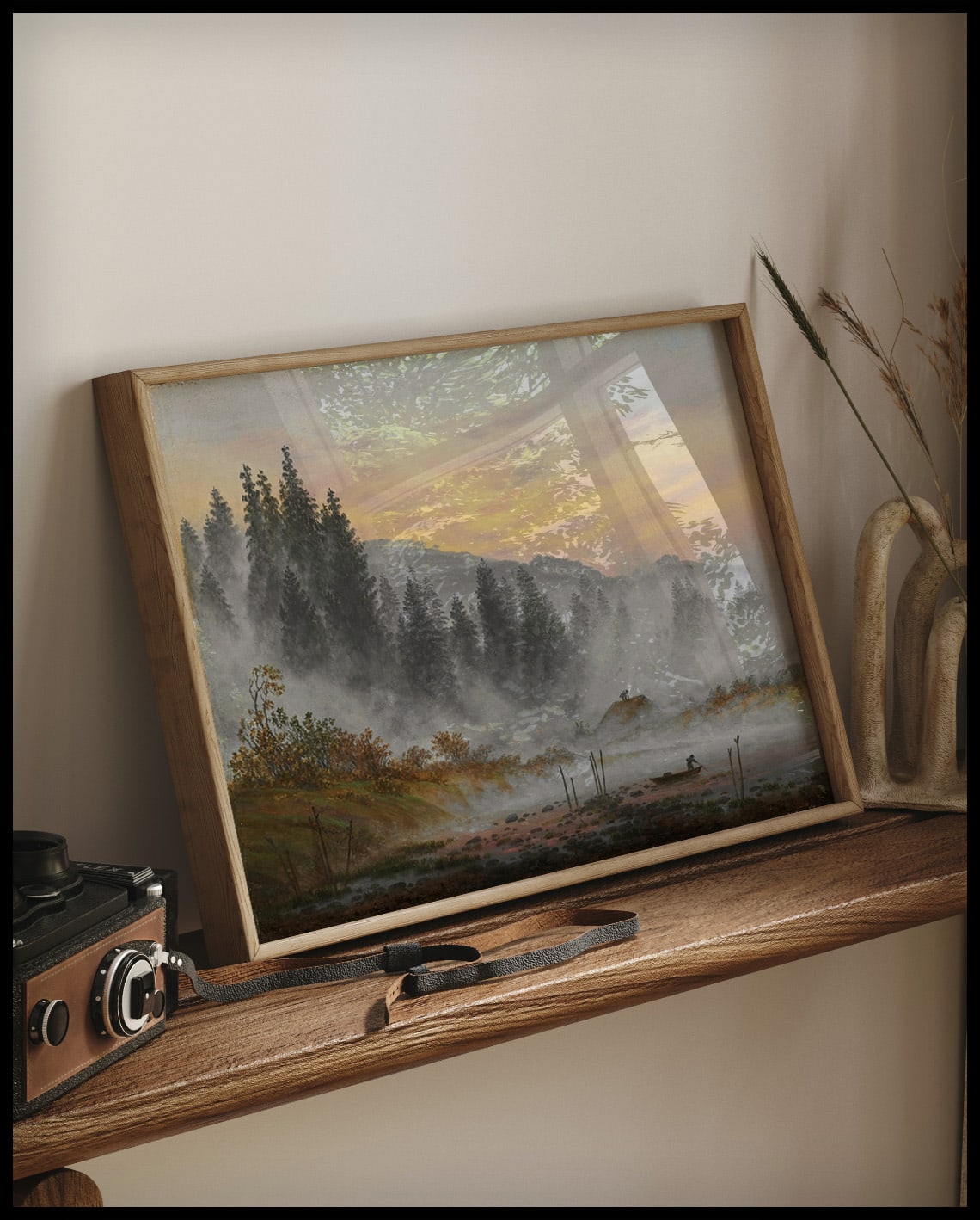Ein gerahmter Kunstdruck von einer Morgenszene mit einer Waldlandschaft, angedeutetem Sonnenaufgang und einem Fischerboot, auf einem Holzregal an die Wand angelehnt