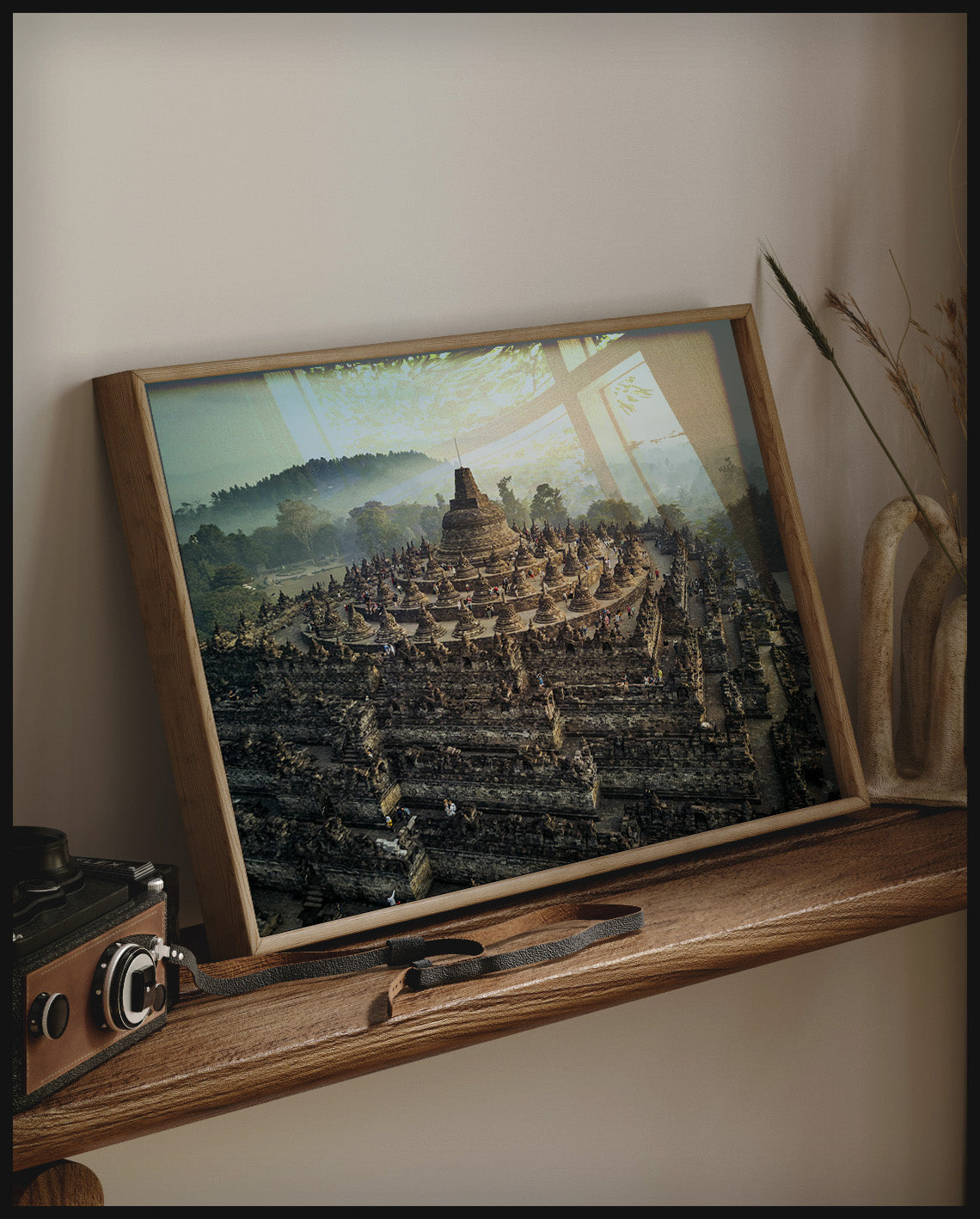 Ein gerahmtes Poster von einer steinernen, mehrstöckigen Tempelanlage, auf einem Holzregal an die Wand angelehnt