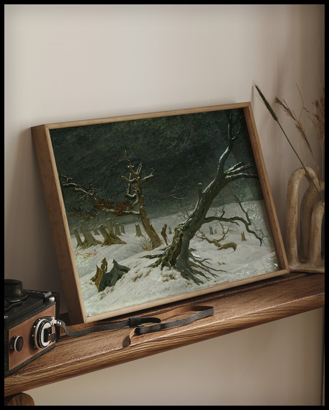 Ein gerahmter Kunstdruck mit einem kahlen Baum und Baumstümpfen inmitten einer schneebedeckten Winterlandschaft, auf einem Holzregal an die Wand angelehnt
