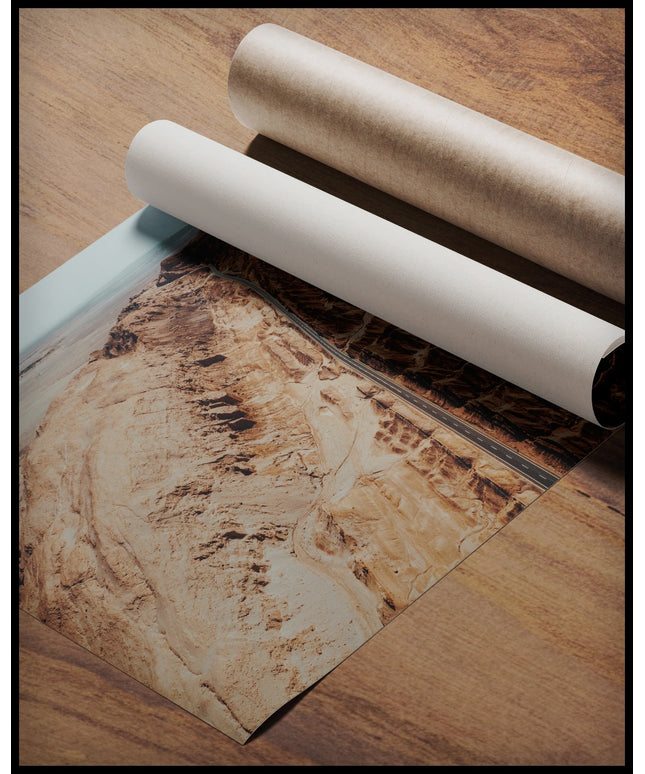 Ein Poster von einer Straße, die durch eine zerklüftete Landschaft in der Atacama-Wüste führt, gerollt auf einer Holzoberfläche liegend