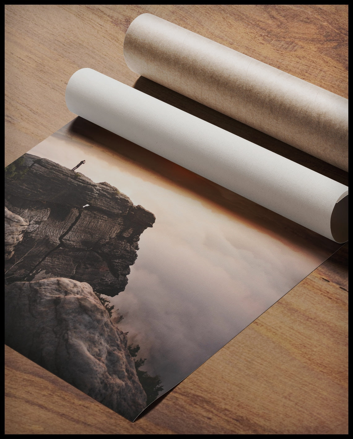 Ein Poster von einem Bergsteiger, der bei Sonnenaufgang auf einer Klippe steht, gerollt auf einer Holzoberfläche liegend