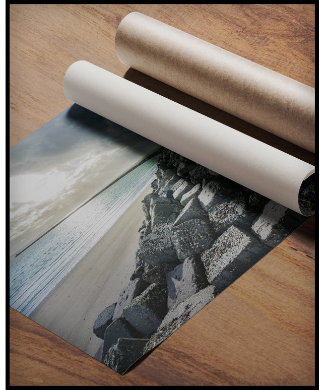 Ein Poster von einem langen Wellenbrecher aus Steinen, der ins Meer ragt, gerollt auf einer Holzoberfläche liegend