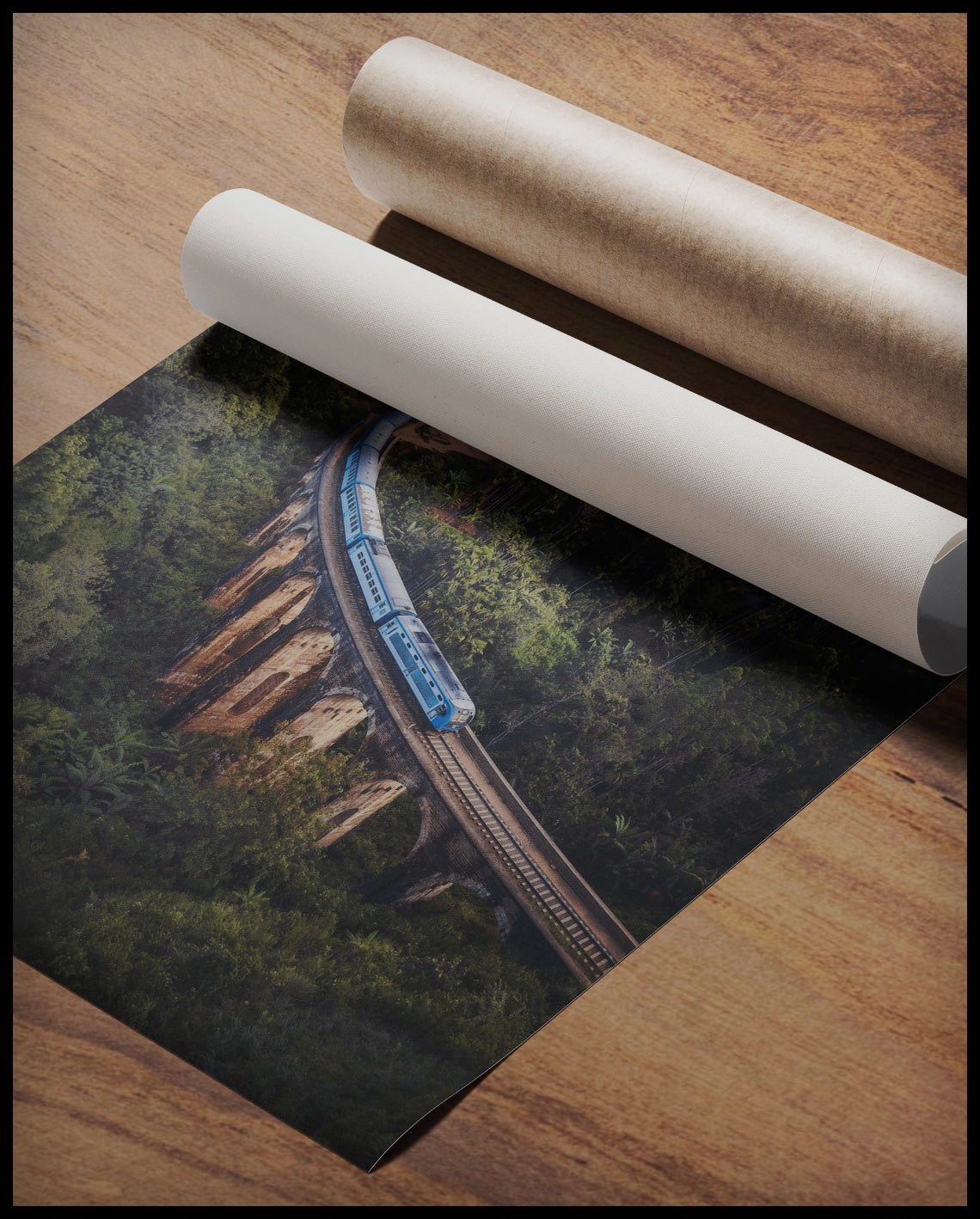 Ein Poster von einem blauen Zug, der über eine alte Brücke inmitten eines grünen Waldes fährt, gerollt auf einer Holzoberfläche liegend