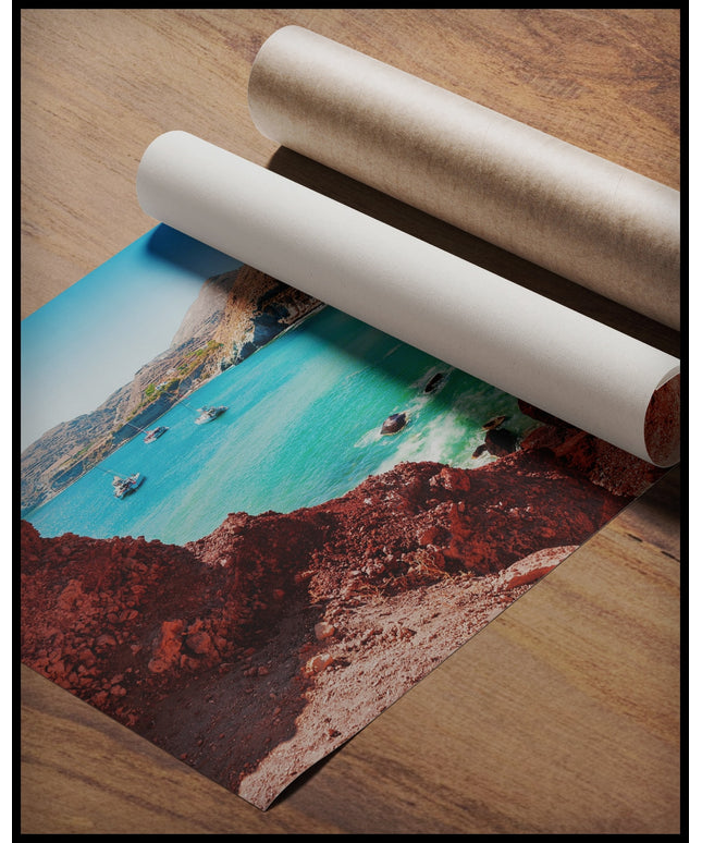 Ein Poster von einer idyllischen Bucht mit klarem, türkisfarbenem Wasser und roten Felsen, gerollt auf einer Holzoberfläche liegend