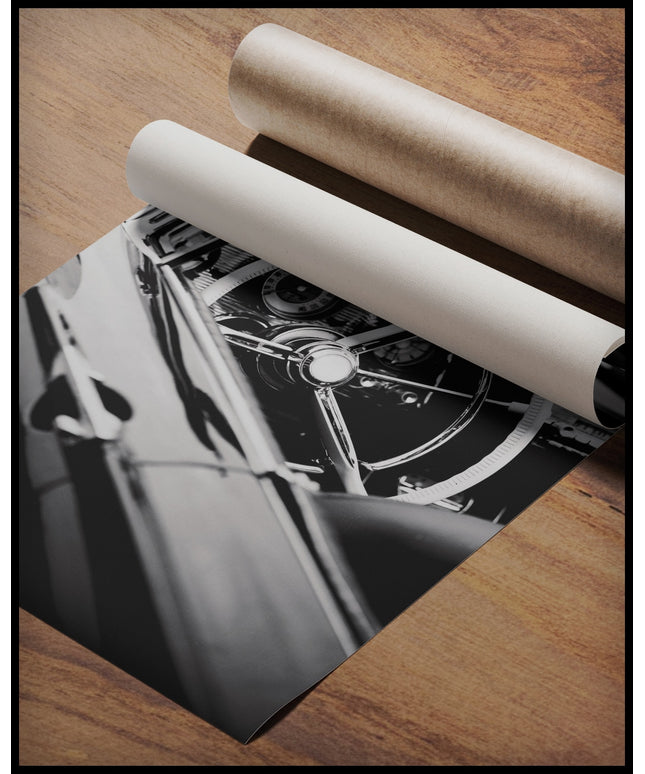 Ein Poster von dem Lenkrad und Armaturenbrett eines klassischen Cabriolets in Schwarz-Weiß, gerollt auf einer Holzoberfläche liegend