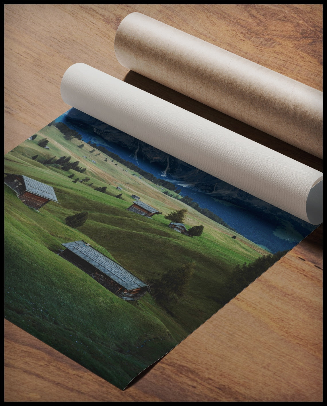 Ein Poster von einer grünen Alm mit kleinen Hütten und den Dolomiten im Hintergrund, gerollt auf einer Holzoberfläche liegend