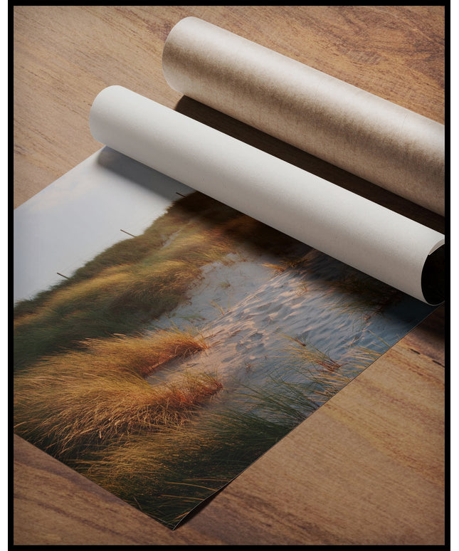Ein Poster von einem Leuchtturm auf Sylt, der hinter grasbedeckten Dünen hervorschaut, gerollt auf einer Holzoberfläche liegend