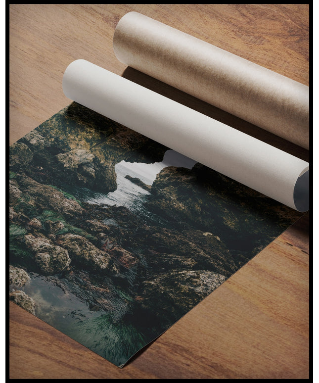 Ein Poster von einer felsigen Küste mit einer natürlichen Felsformation, die ein Fenster zum Meer bildet, gerollt auf einer Holzoberfläche liegend