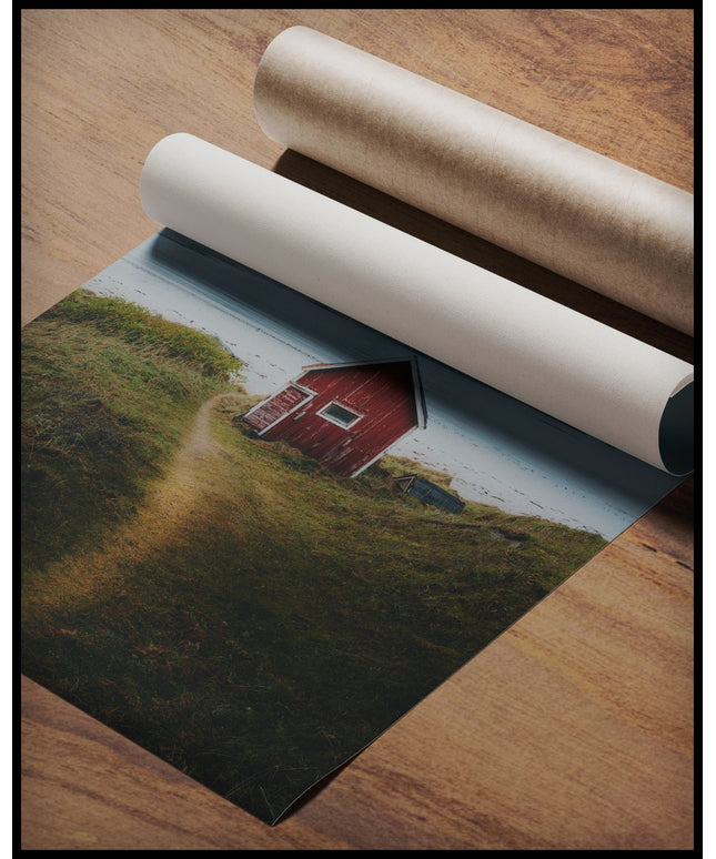 Ein Poster von einem kleinen roten Haus am Seeufer mit Bergen im Hintergrund, gerollt auf einer Holzoberfläche liegend