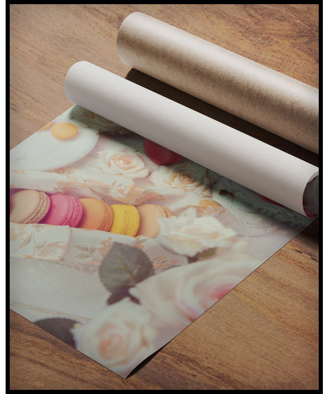 Ein Poster von bunten Macarons, arrangiert auf einem Tisch mit rosa Rosen und weißem Porzellan, gerollt auf einer Holzoberfläche liegend