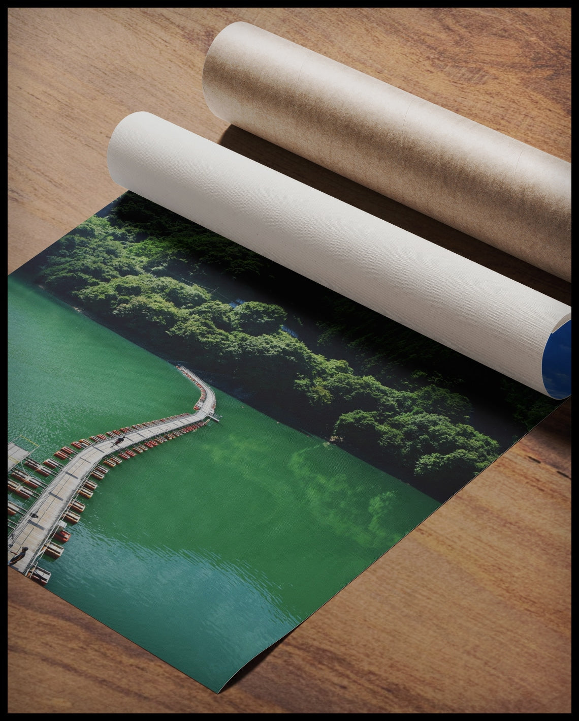 Ein Poster von einer schwimmenden Brücke auf einem grünlichen See, die in einen Wald hinein führt, gerollt auf einer Holzoberfläche liegend