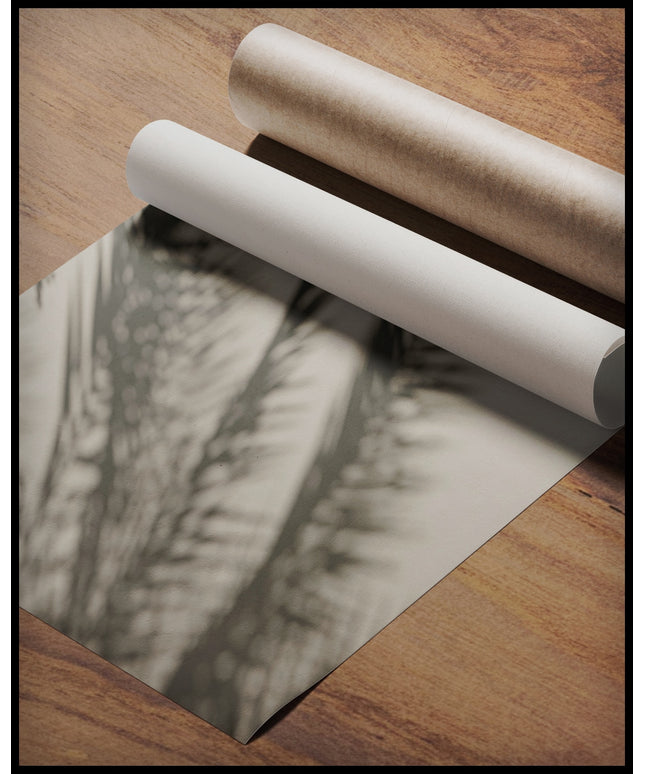 Ein Poster vom Schatten mehrerer Palmenblätter auf einer beigen Wand, gerollt auf einer Holzoberfläche liegend