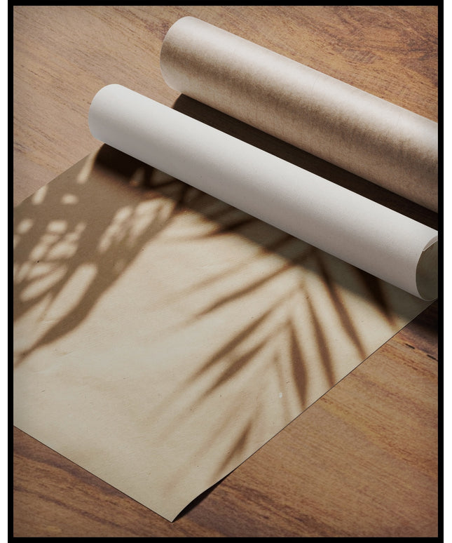 Ein Poster vom Schatten einzelner Palmenblätter auf einer beigefarbenen Häuserfassade, gerollt auf einer Holzoberfläche liegend