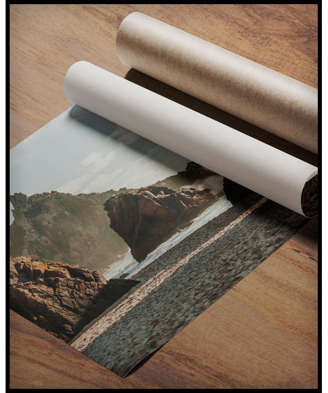 Ein Poster von hohen Felsformationen im Meer an einem Sandstrand, gerollt auf einer Holzoberfläche liegend