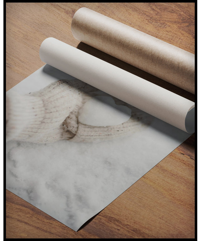 Ein Poster von einer behandschuhten Hand, die ein kleines Herz aus Schnee hält, gerollt auf einer Holzoberfläche liegend