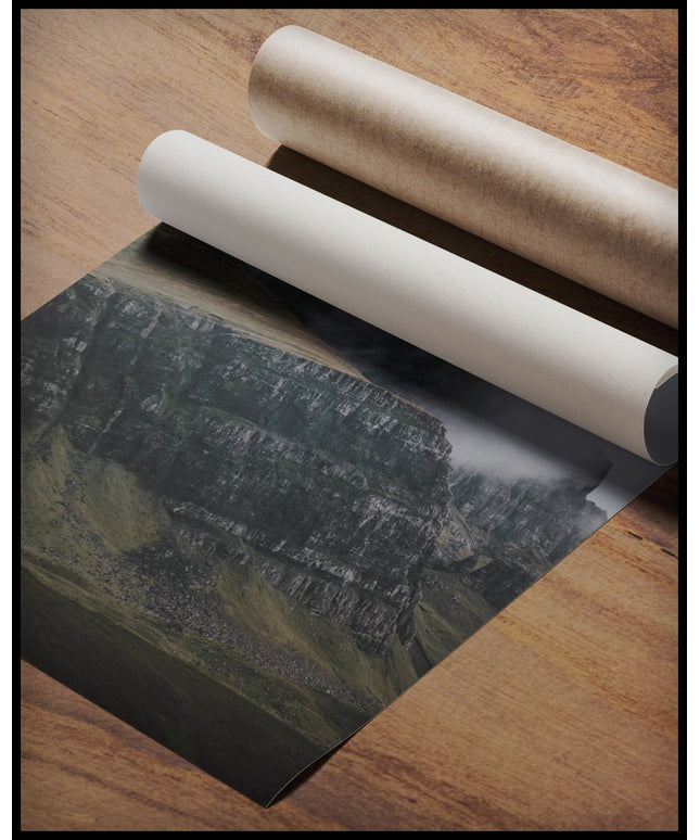 Ein Poster von einem steilen Abhang eines Berges, der von Gras bedeckt und von Nebel umschlungen ist, gerollt auf einer Holzoberfläche liegend