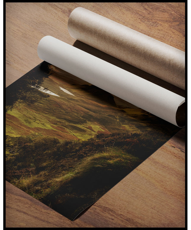 Ein Poster von einer kargen, grünen Berglandschaft im Sonnenuntergang, gerollt auf einer Holzoberfläche liegend