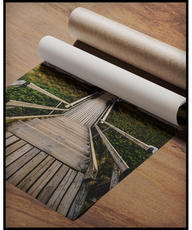 Ein Poster von einem Holzsteg mit einer Treppe, der durch Dünen zum Strand führt, gerollt auf einer Holzoberfläche liegend