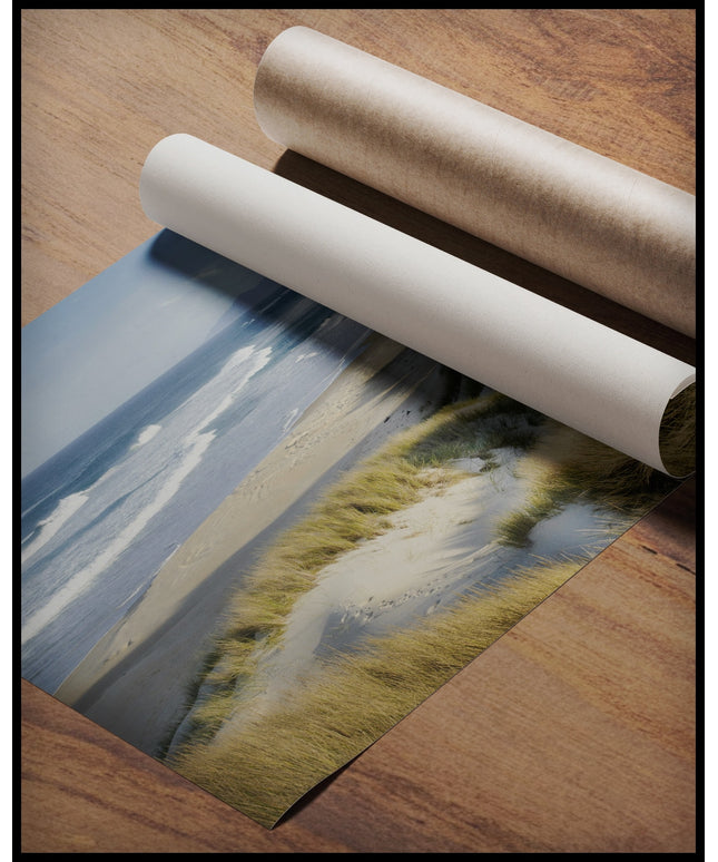 Ein Poster vom Meerblick über Dünen und Strand, gerollt auf einer Holzoberfläche liegend