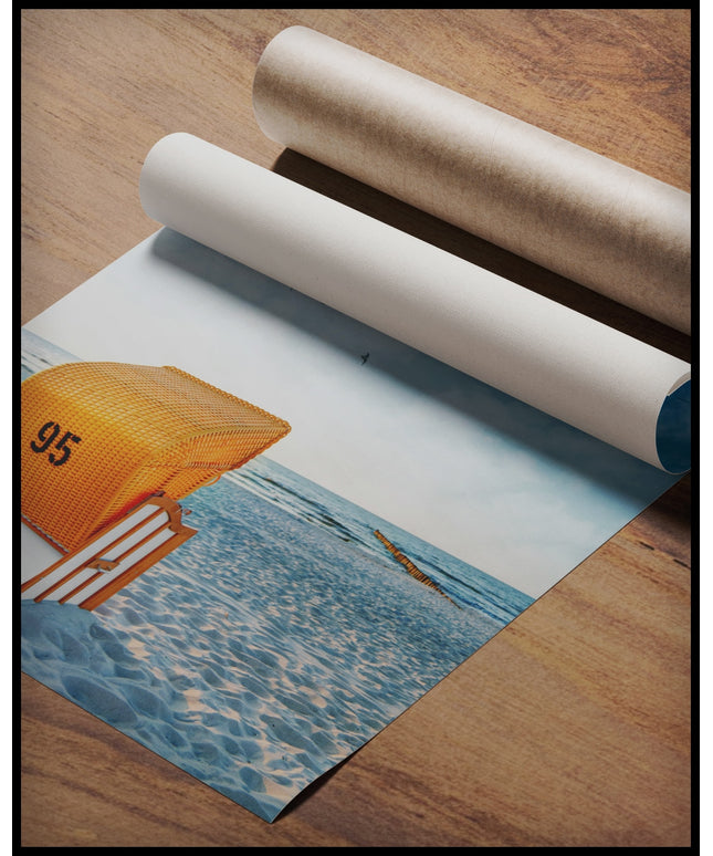 Ein Poster von einem orangenen Strandkorb am Strand der in Richtung Meer gerichtet ist, gerollt auf einer Holzoberfläche liegend