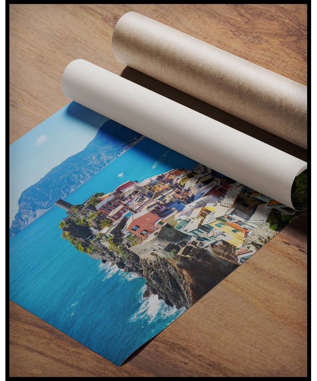 Ein Poster von einer bunten Küstenstadt die auf Klippen vor einem blauen Meer und einer Berglandschaft erbaut wurde, gerollt auf einer Holzoberfläche liegend