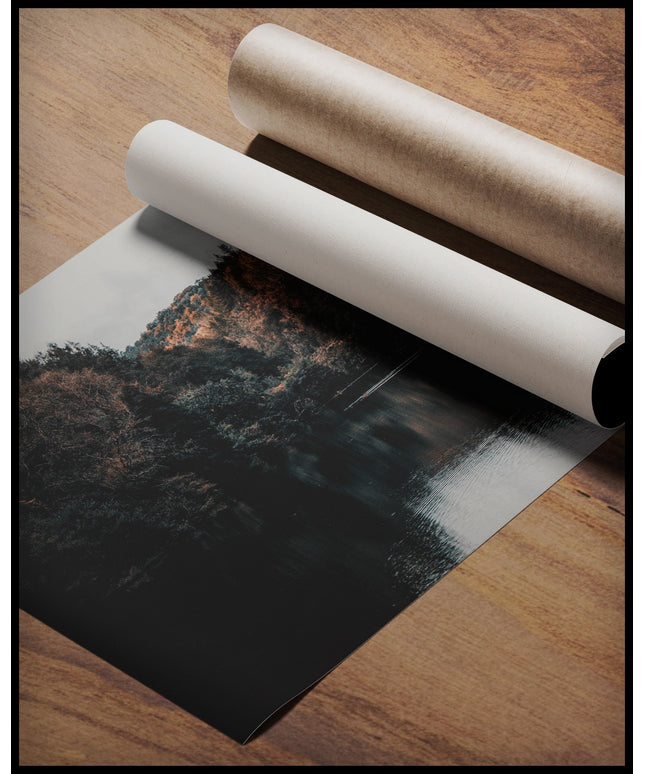 Ein Poster von einem dunklen See der von dunklen Nadelbäumen umringt ist, gerollt auf einer Holzoberfläche liegend