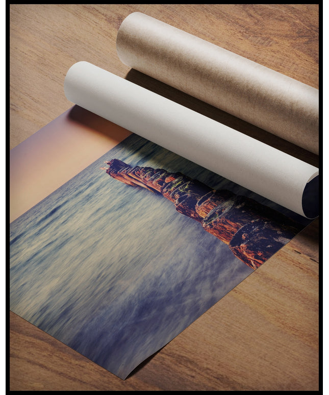 Ein Poster von einem hölzernen Wellenbrecher der in das Meer hinein ragt, gerollt auf einer Holzoberfläche liegend