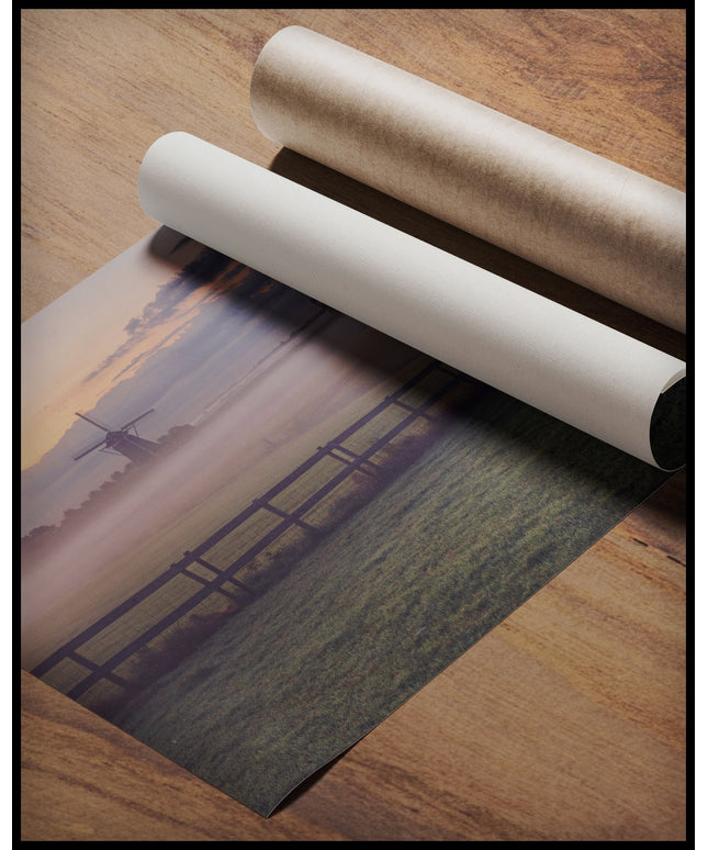 Ein Poster von einer nebligen Wiese und einem Zaun, hinter denen sich Windmühlen verbergen, gerollt auf einer Holzoberfläche liegend