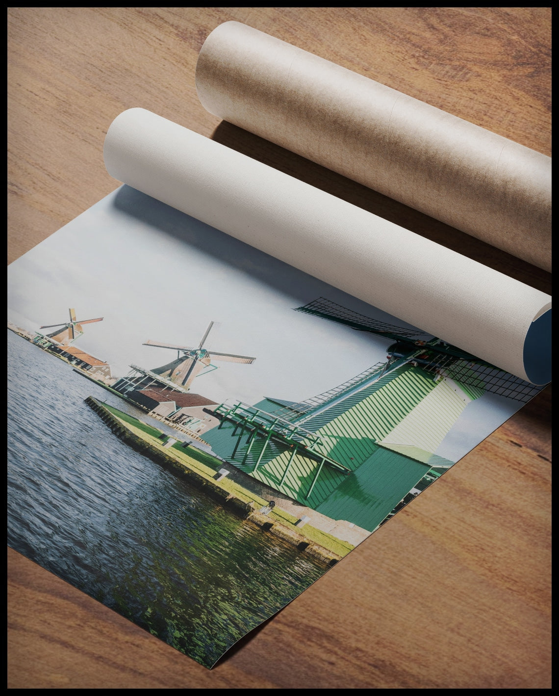 Ein Poster von drei Windmühlen aus Holz die am Wasser stehen, gerollt auf einer Holzoberfläche liegend