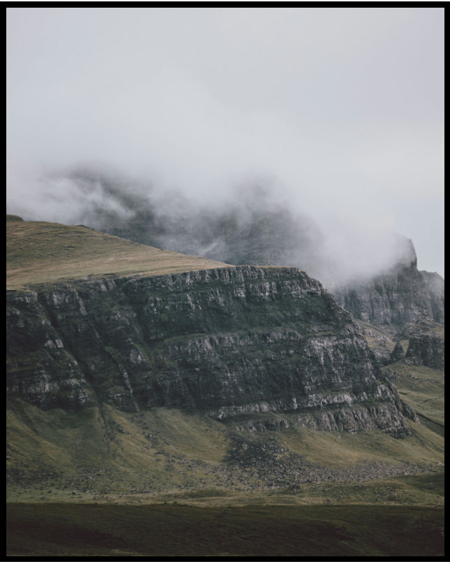 Ein Poster von einem steilen Abhang eines Berges, der von Gras bedeckt und von Nebel umschlungen ist.