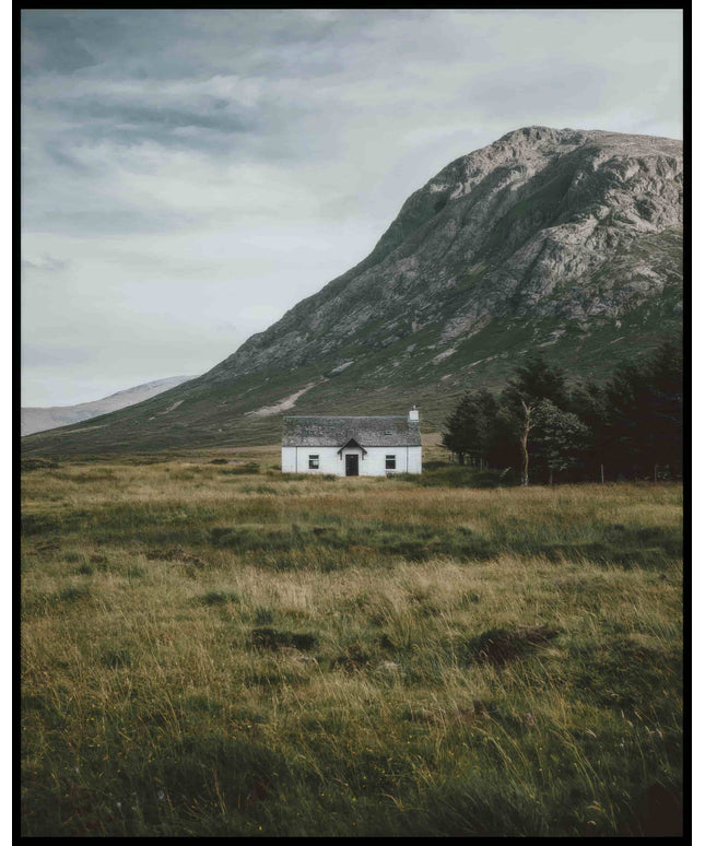 Ein Poster von einer weißen Holzhütte auf einer Wiese vor einem Berg.