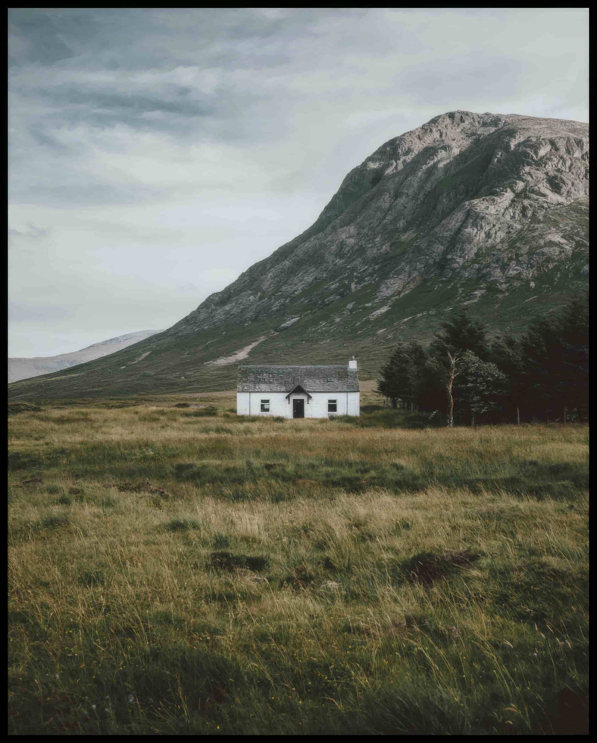 Ein Poster von einer weißen Holzhütte auf einer Wiese vor einem Berg.