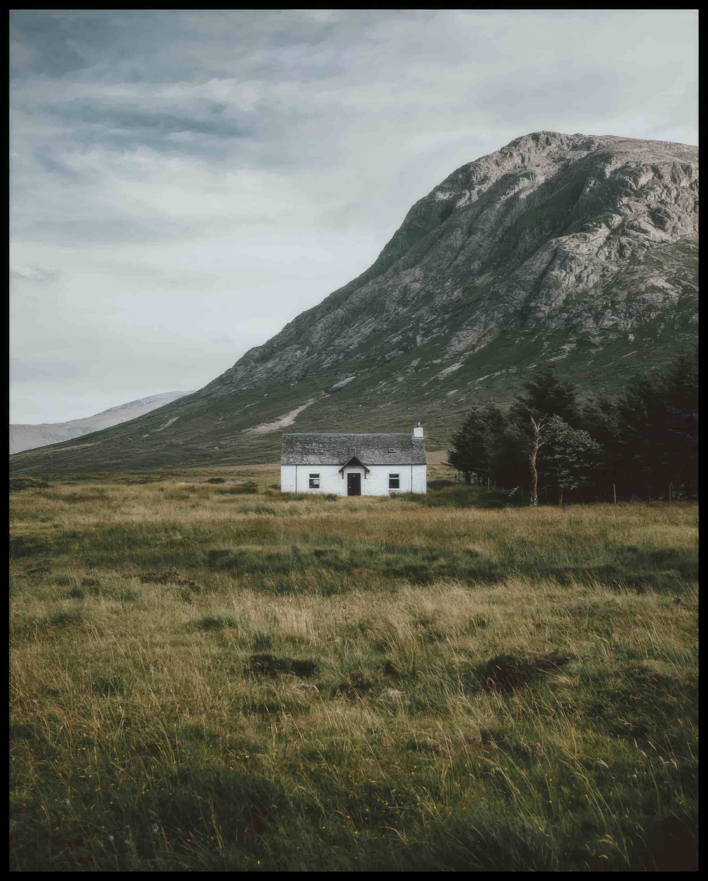 Ein Poster von einer weißen Holzhütte auf einer Wiese vor einem Berg.