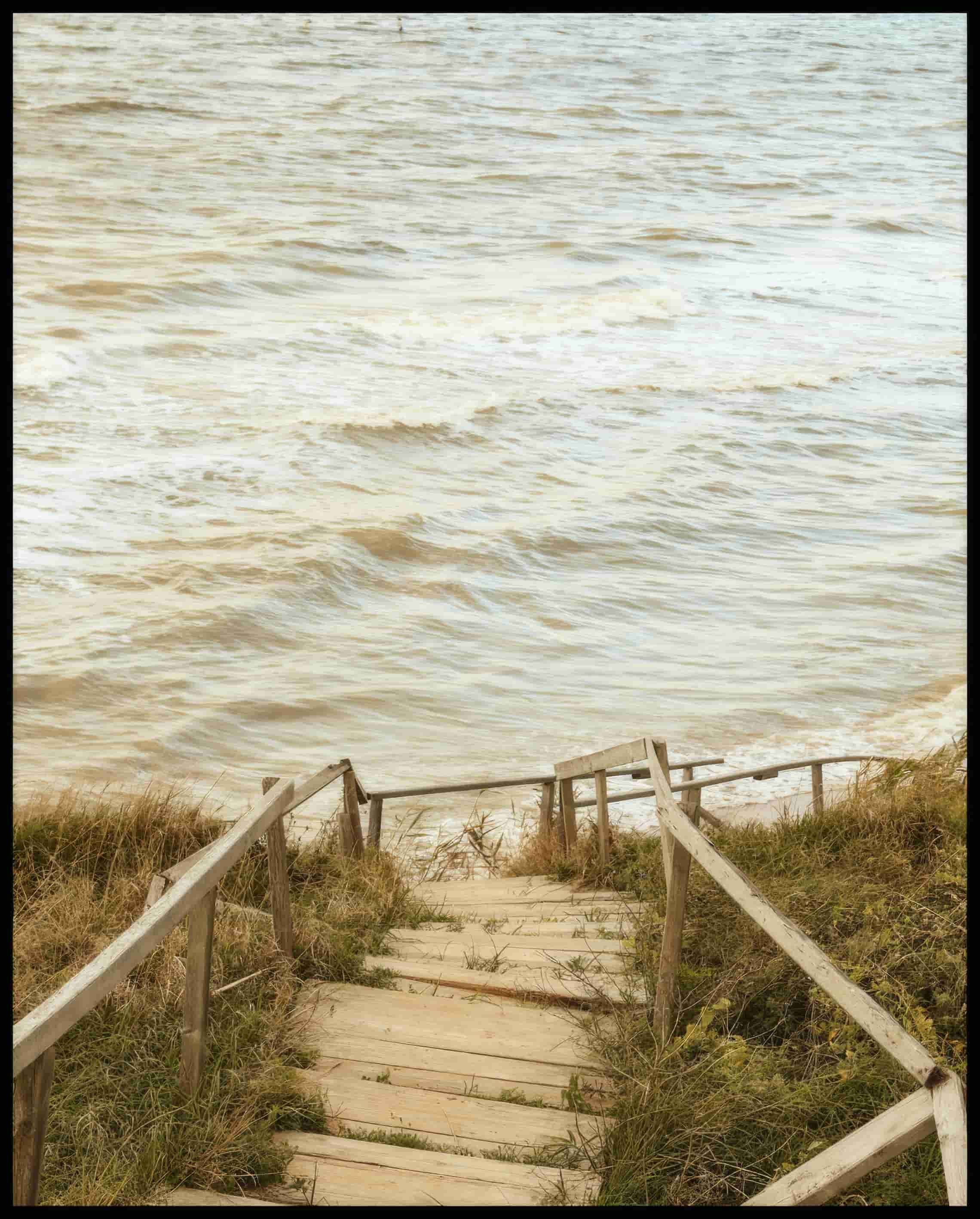 Ein Poster von einem Holzsteg mit einer Treppe, der durch Dünen zum Strand führt.