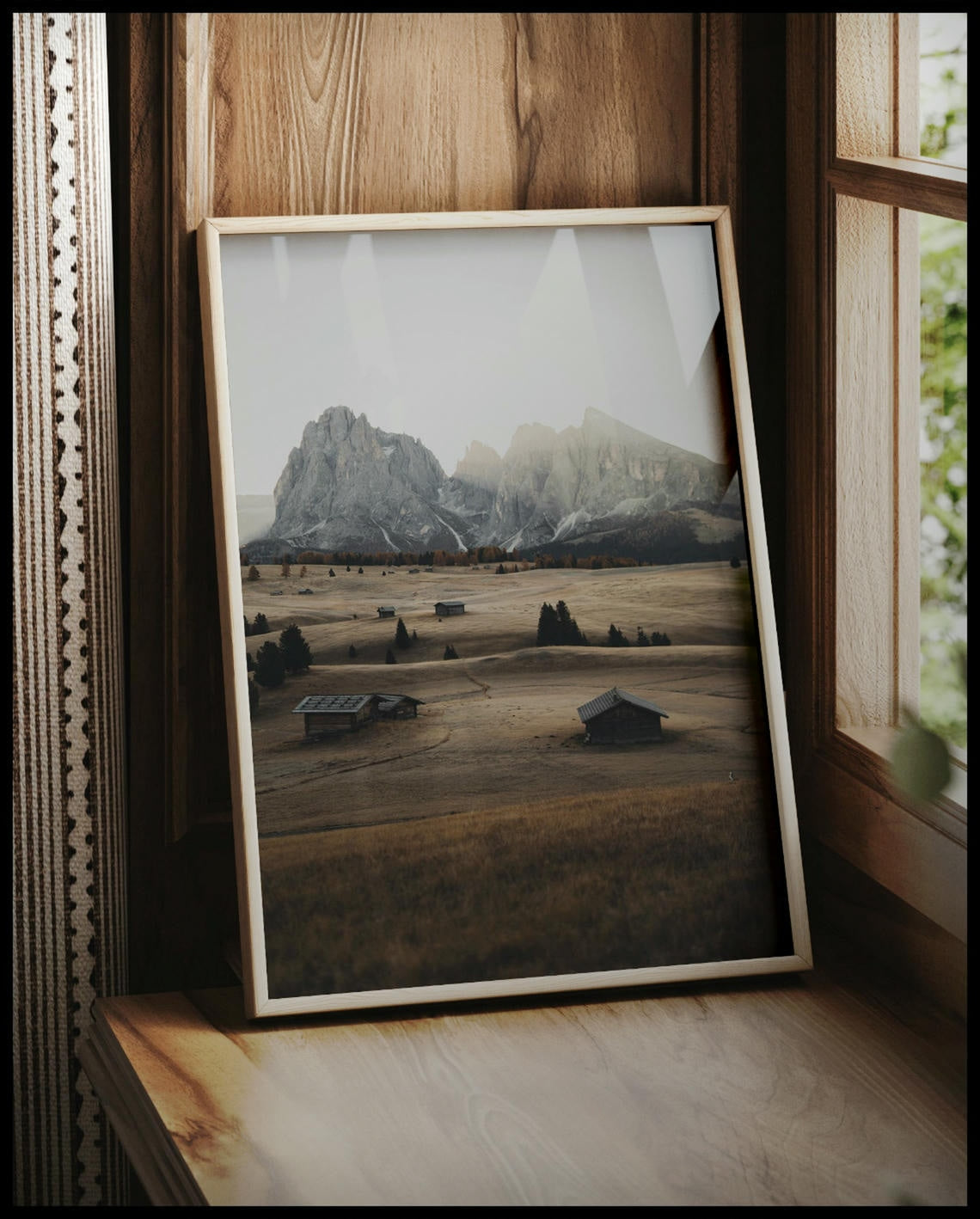 Ein gerahmtes Poster von einer Alm in den Dolomiten bei Sonnenaufgang, vor einem Fenster an die Wand angelehnt