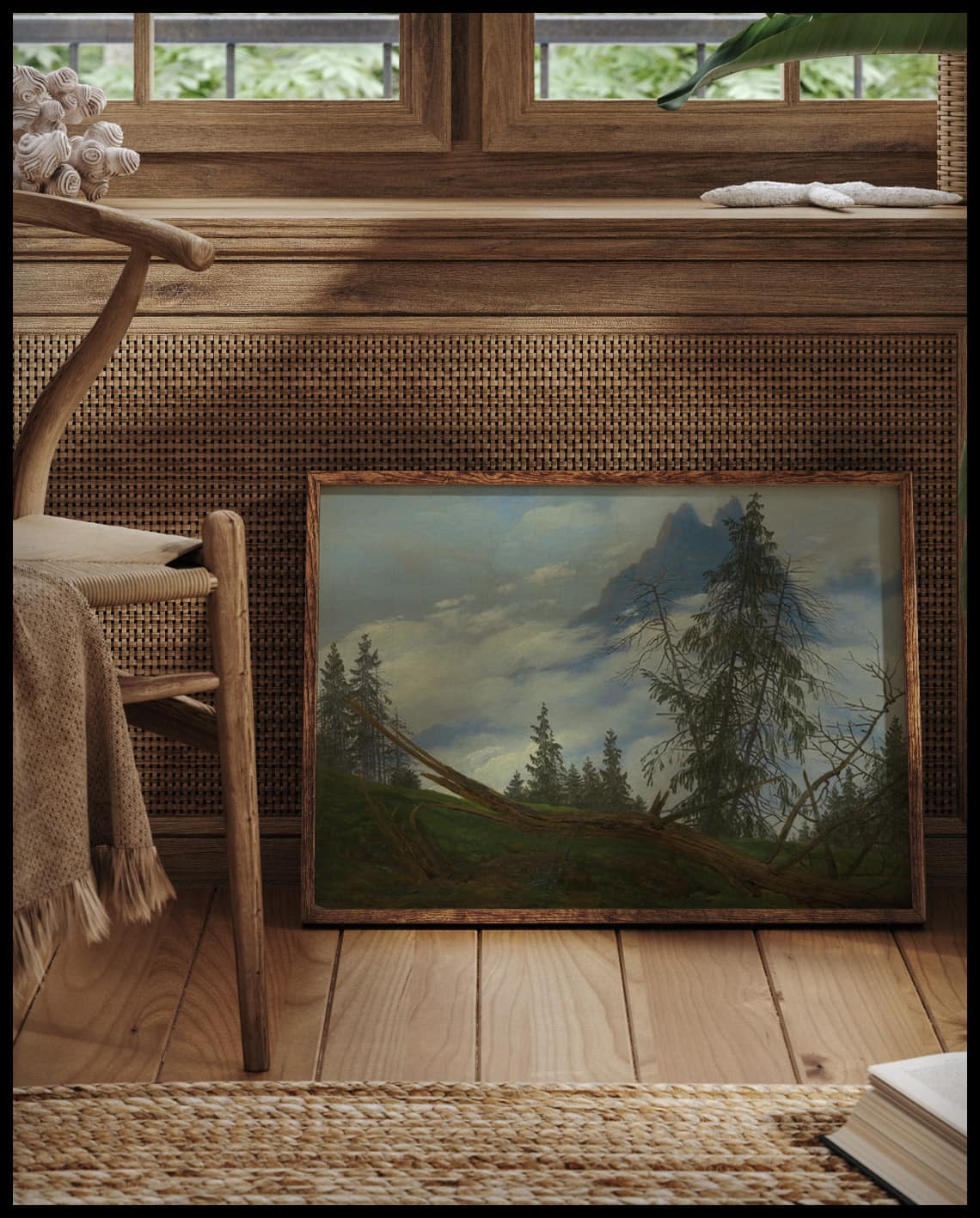 Ein gerahmter Kunstdruck von einer Waldszene auf einem Berggipfel, vor einem Fenster an die Wand angelehnt