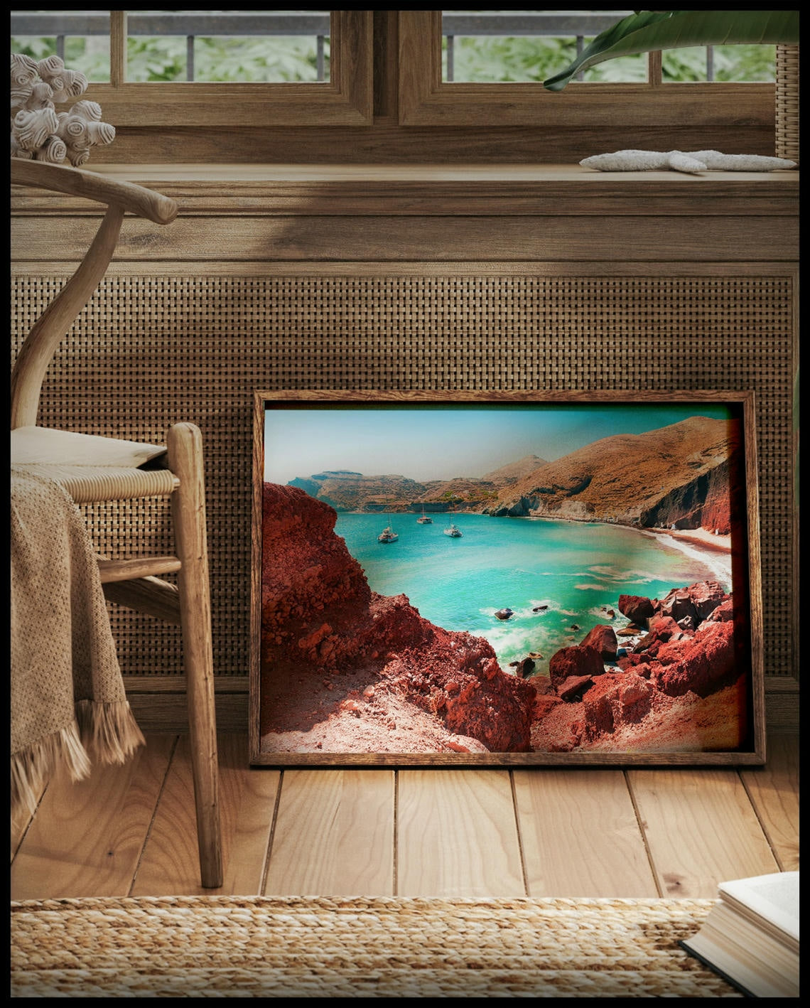 Ein gerahmtes Poster von einer idyllischen Bucht mit klarem, türkisfarbenem Wasser und roten Felsen, vor einem Fenster an die Wand angelehnt