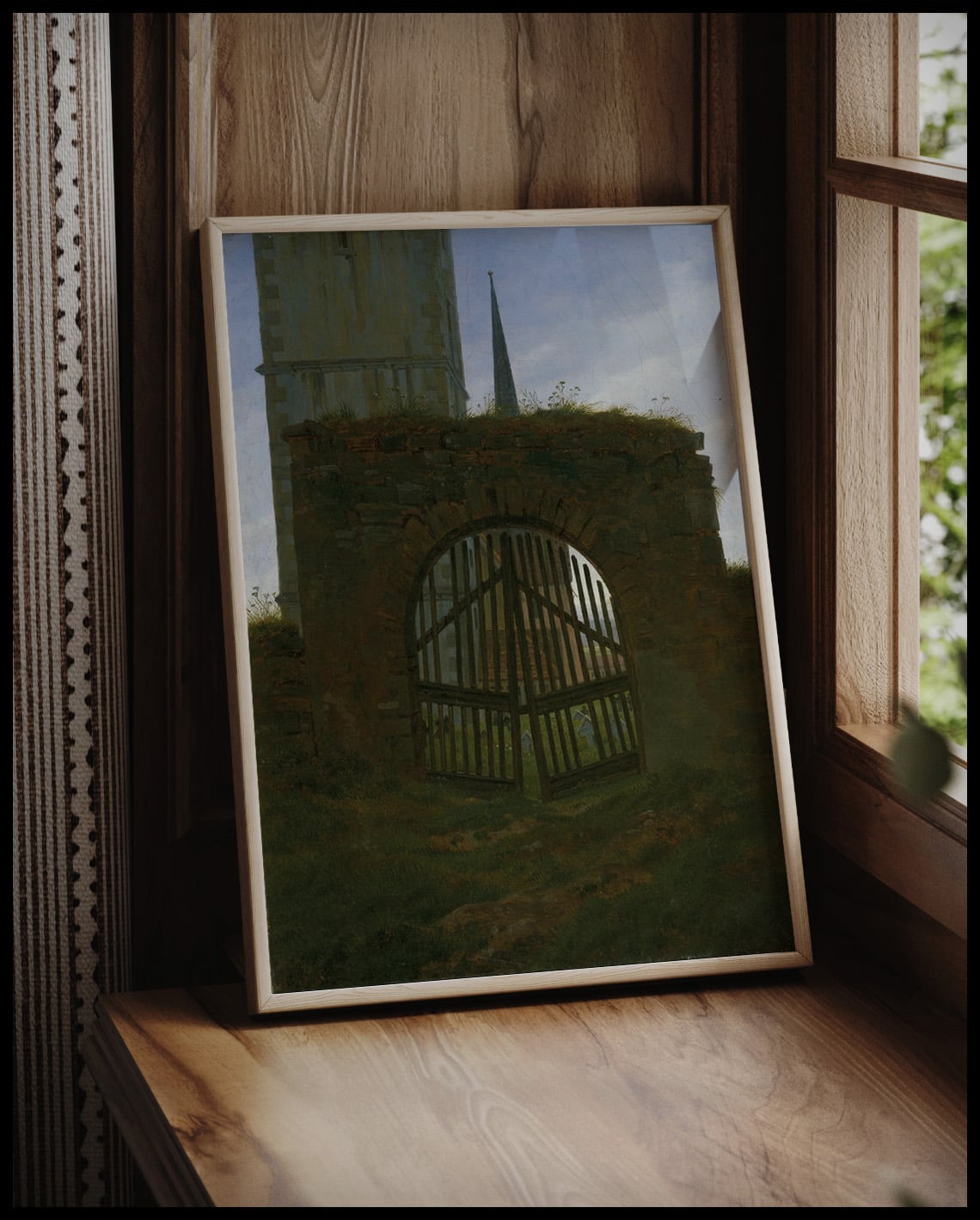 Ein gerahmter Kunstdruck eines Friedhofstors vor einem Fenster an die Wand angelehnt