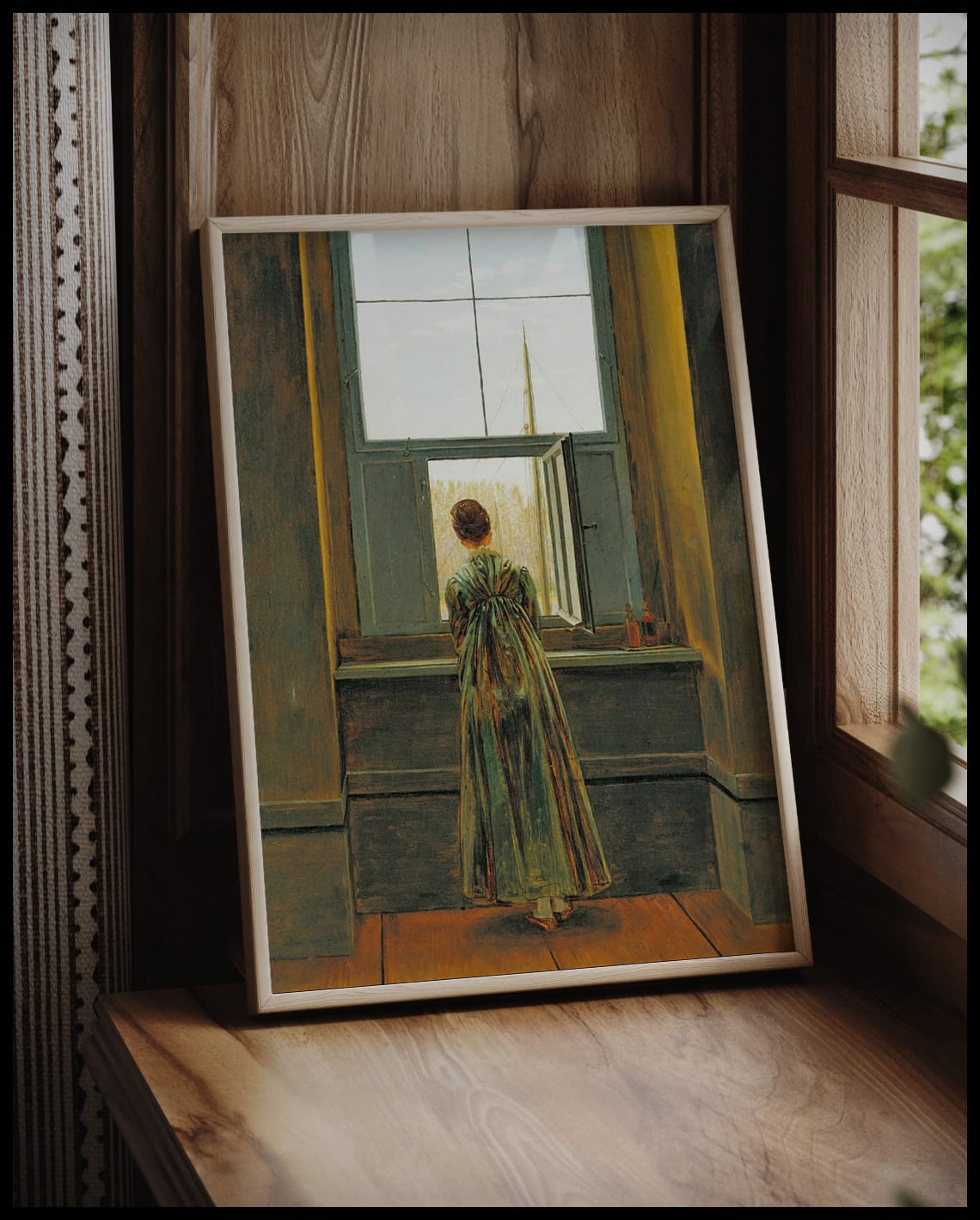Ein gerahmter Kunstdruck einer Frau, die in einem langen Kleid aus einem geöffneten Fenster schaut, vor einem Fenster an die Wand angelehnt