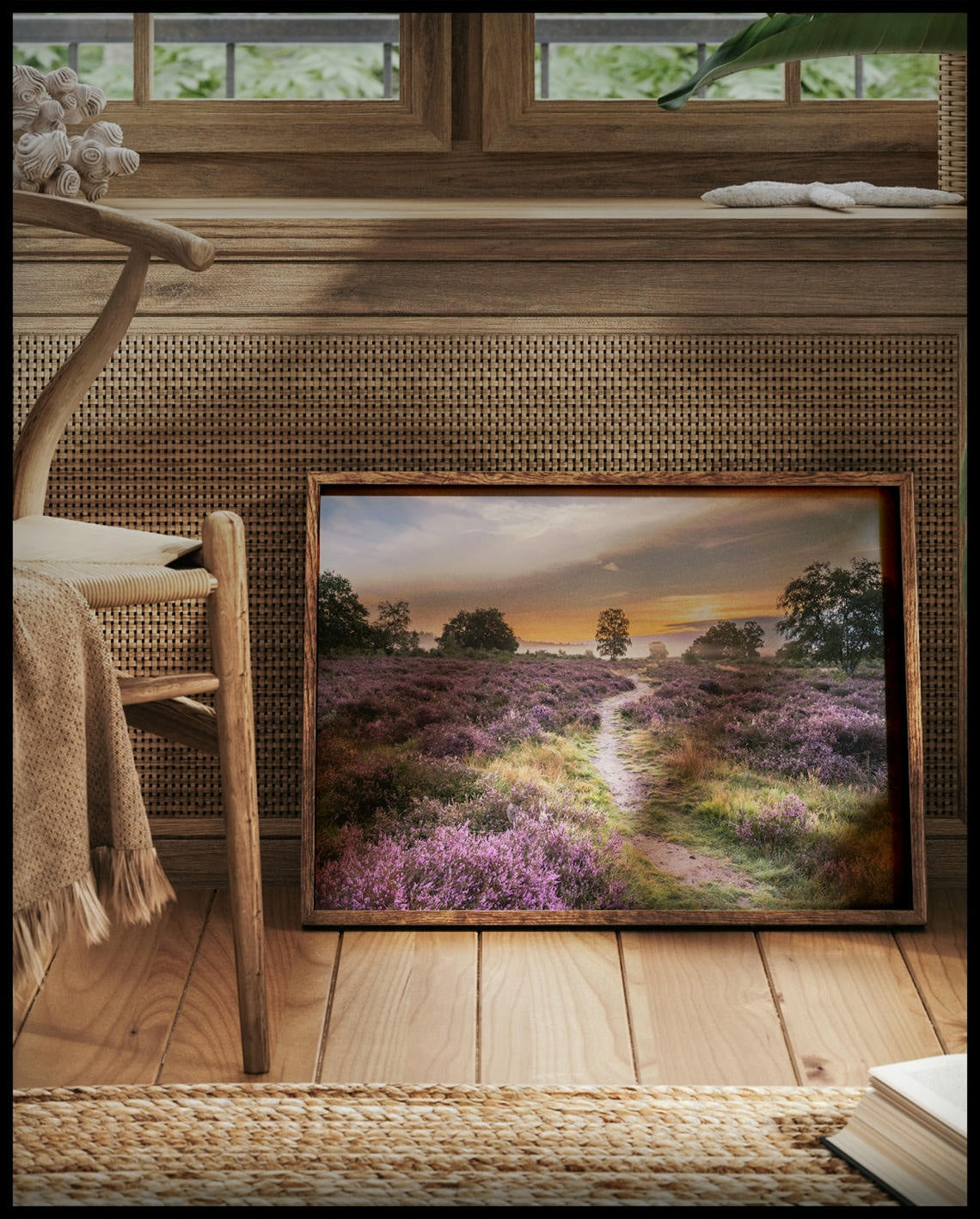 Ein gerahmtes Poster von einer Heidefläche mit lila Blumen im Sonnenuntergang, vor einem Fenster an die Wand angelehnt