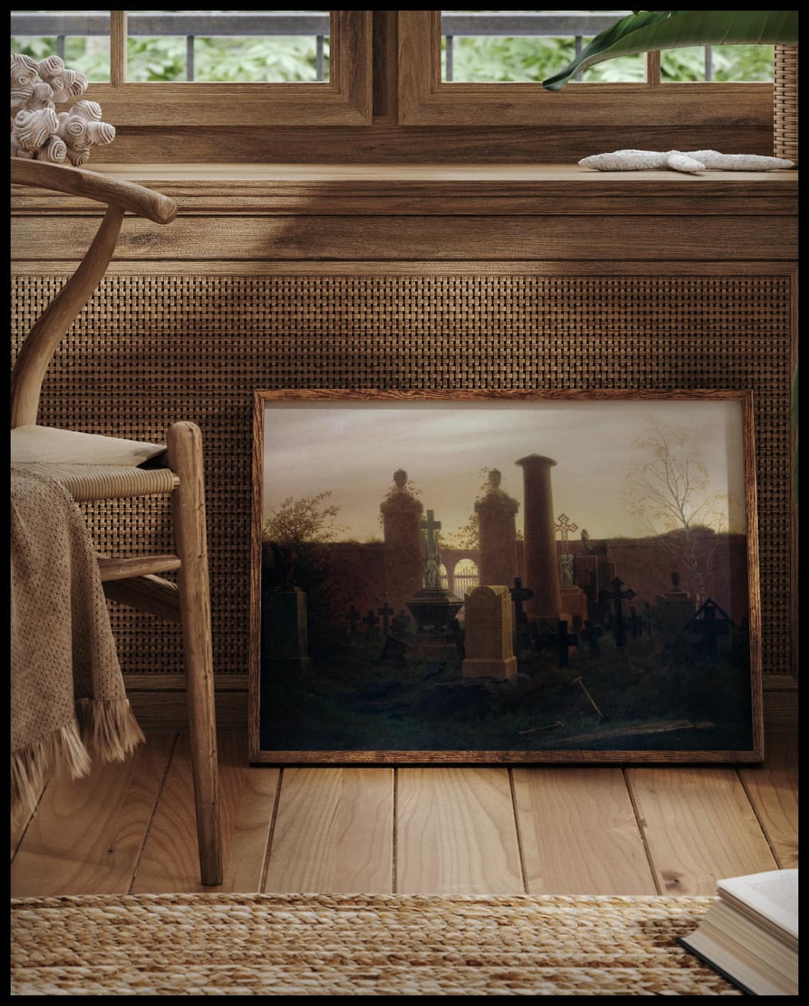 Ein gerahmter Kunstdruck von einem Friedhof mit einigen Gräbern und dem Sonnenuntergang im Hintergrund, vor einem Fenster an die Wand angelehnt