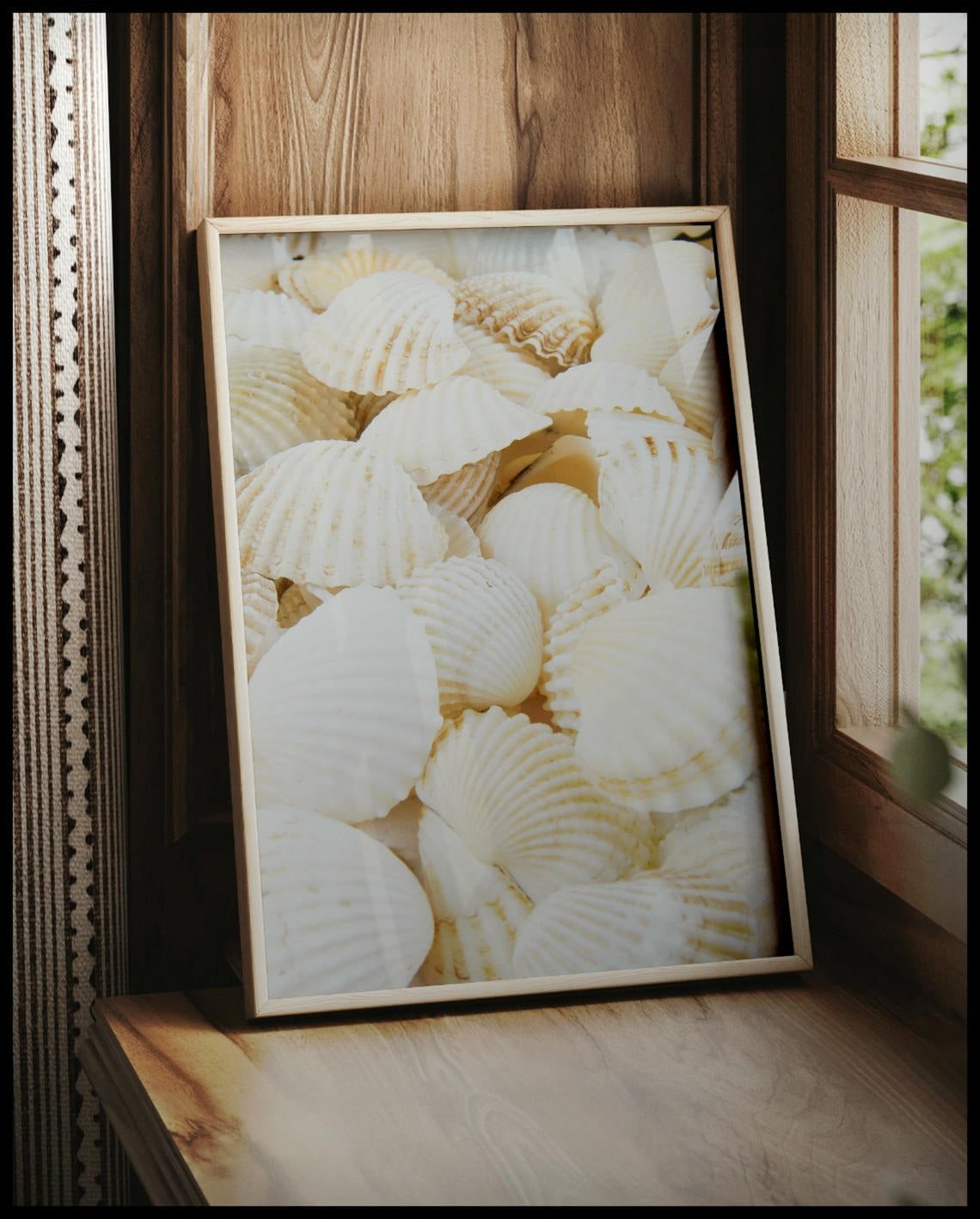 Ein gerahmtes Poster von weißen Muscheln, vor einem Fenster an die Wand angelehnt