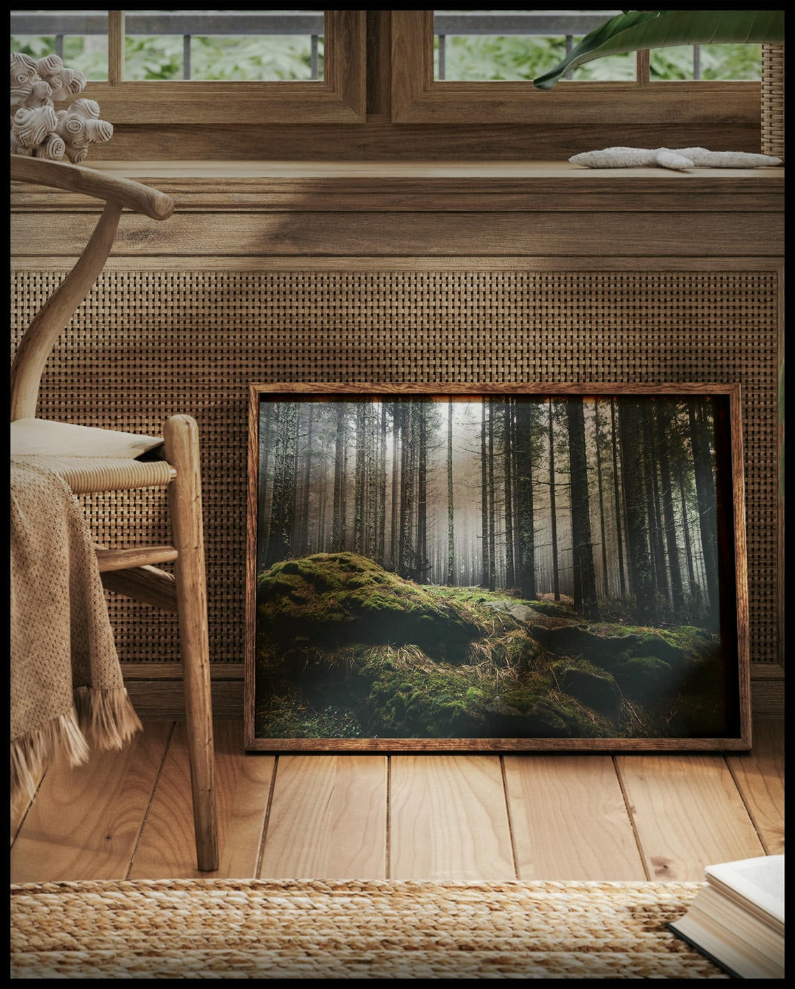 Ein gerahmtes Poster von einem nebeligen Wald mit moosbedeckten Steinen im Vordergrund, vor einem Fenster an die Wand angelehnt